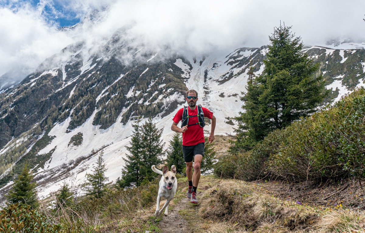 Scott trail running toward the camera with his dog on a mountain path above Chamonix, snow-covered peaks behind